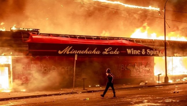 Seorang demonstran berjalan di sebelah toko yang terbakar di Amerika Serikat.(Getty Images)/detik.com