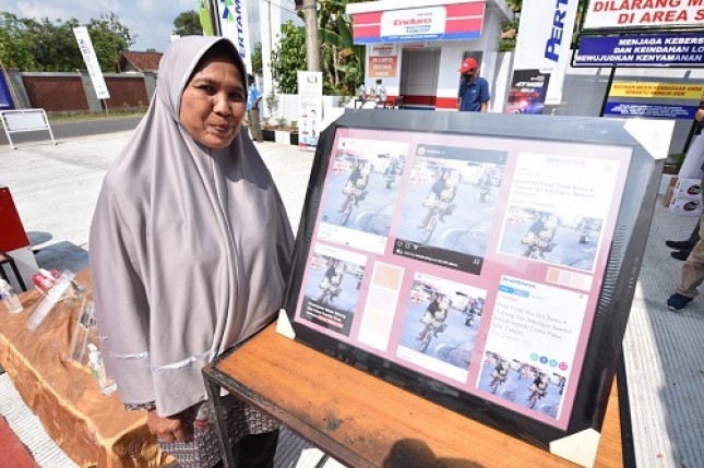 Neni Penjual Gas LPG 3 kg berpose dengan bingkai foto berisi foto kegiatannya saat acara Peresmian Pertashop 3P.46309 di Desa Sukajaya, Kabupaten Ciamis, Jawa Barat, pada minggu (13/6/2021). (Foto: Adityo) Pen