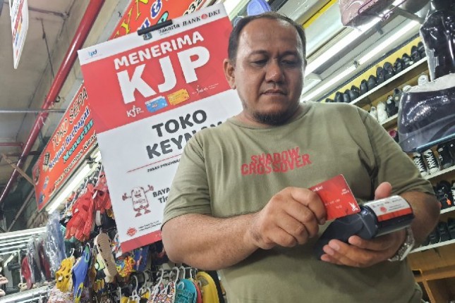 Pemilik toko menggesekan kartu debit bank DKI untuk pembayaran suatu barang dagangan 